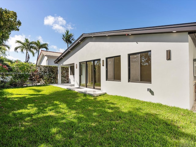 rear view of house with a yard, a patio, and stucco siding