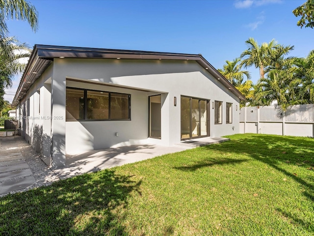 rear view of property with a yard, a patio area, fence, and stucco siding