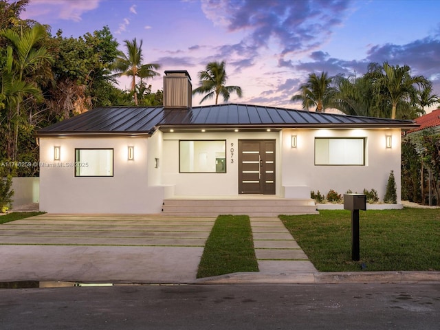 view of front facade with metal roof, a standing seam roof, and stucco siding