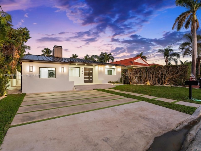 back of property at dusk featuring metal roof, a yard, stucco siding, a standing seam roof, and a chimney