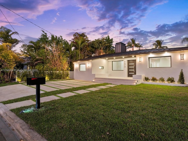 single story home with a chimney, metal roof, a standing seam roof, a front lawn, and stucco siding