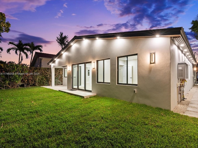 back of house featuring a patio, a lawn, and stucco siding