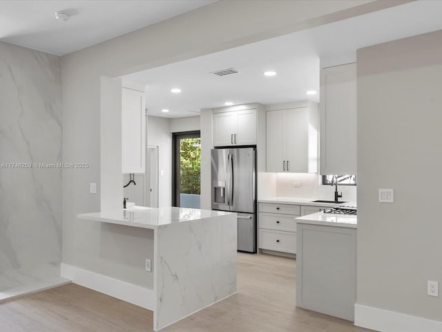 kitchen with stainless steel fridge, visible vents, a peninsula, light wood-style floors, and a sink