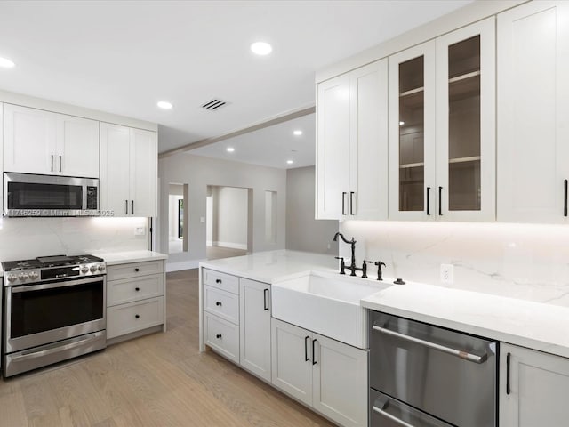 kitchen with a sink, visible vents, appliances with stainless steel finishes, decorative backsplash, and light wood finished floors