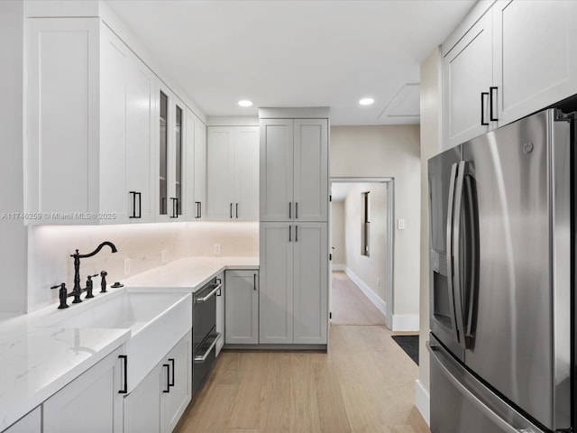 kitchen featuring a sink, stainless steel fridge with ice dispenser, decorative backsplash, light wood finished floors, and glass insert cabinets