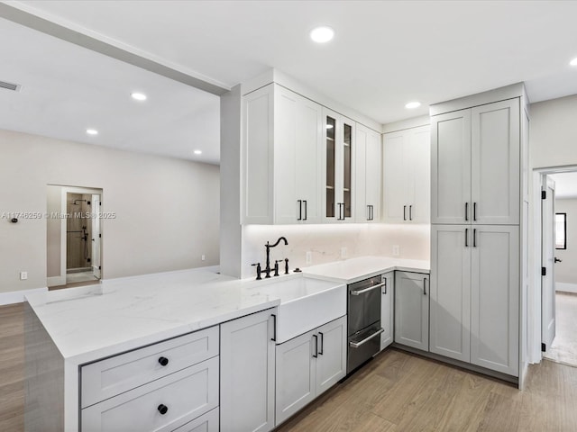 kitchen featuring light stone counters, recessed lighting, light wood-style flooring, glass insert cabinets, and a sink