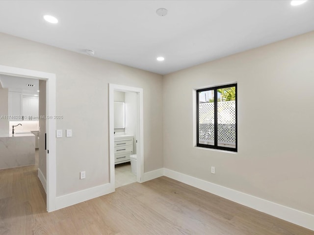 unfurnished bedroom featuring baseboards, recessed lighting, ensuite bath, and light wood-style floors