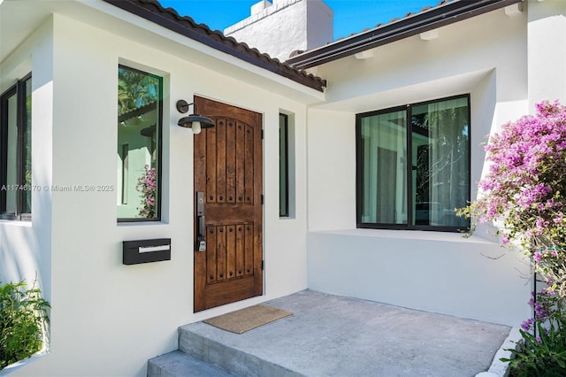 view of exterior entry featuring a tiled roof, a chimney, and stucco siding