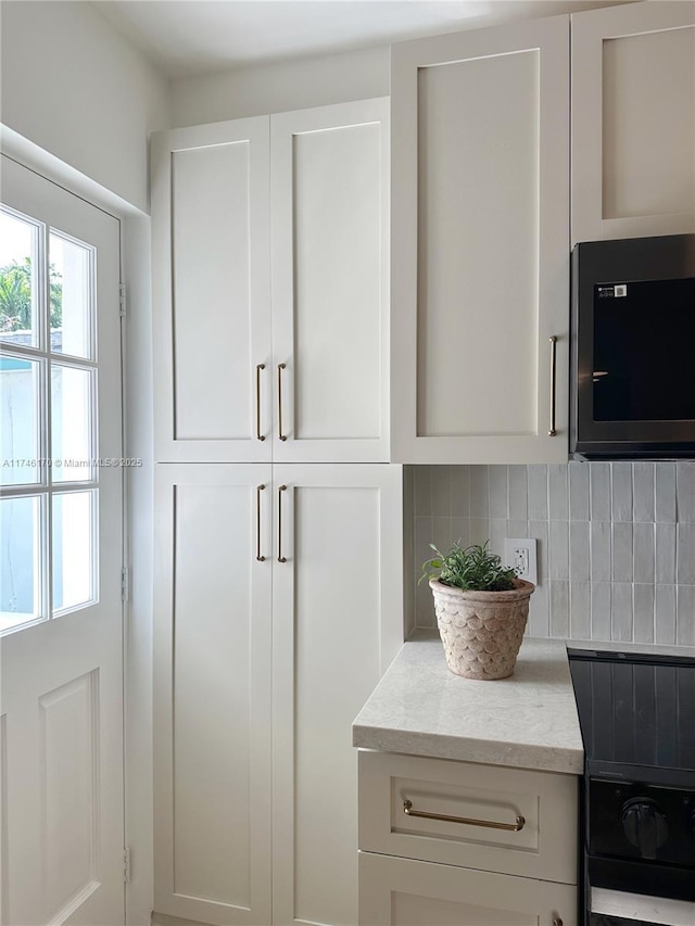 interior details featuring light stone countertops, range, white cabinets, and decorative backsplash