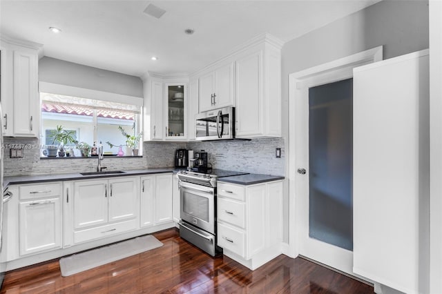 kitchen with stainless steel appliances, dark countertops, glass insert cabinets, white cabinets, and a sink