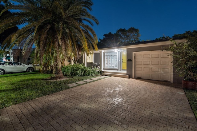 view of front of house with decorative driveway, a yard, an attached garage, and stucco siding