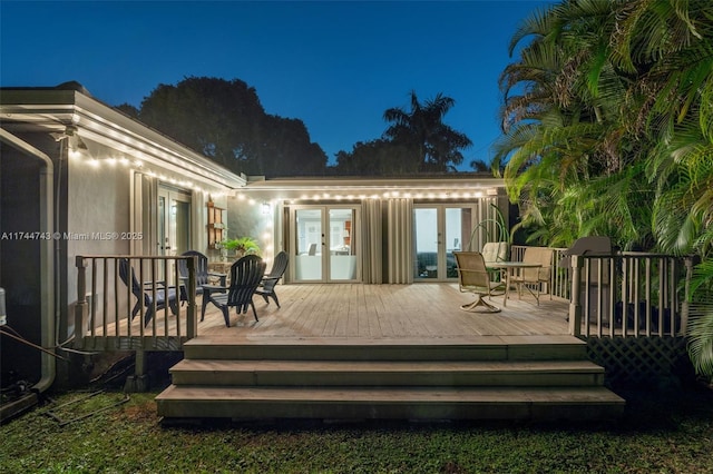 back of house at twilight with french doors, a deck, and stucco siding