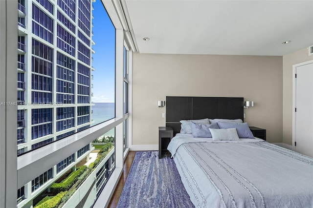 bedroom featuring dark hardwood / wood-style flooring, a wall of windows, and a water view