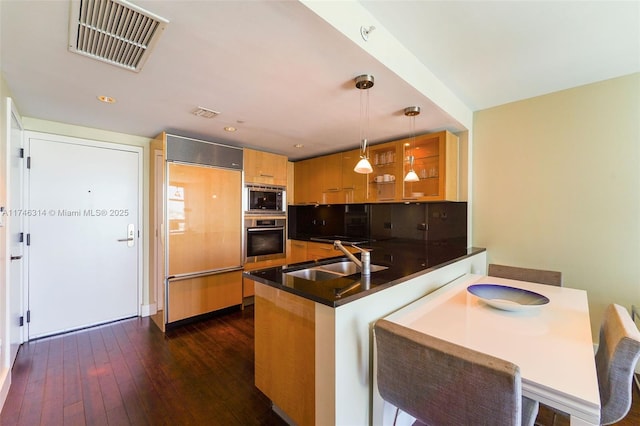 kitchen with sink, hanging light fixtures, dark hardwood / wood-style floors, built in appliances, and kitchen peninsula