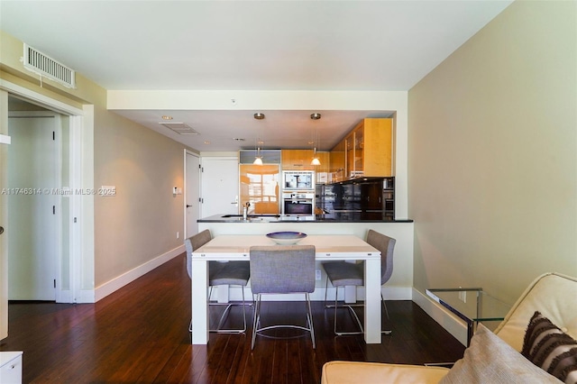 kitchen with dark wood-type flooring, sink, a breakfast bar area, appliances with stainless steel finishes, and pendant lighting