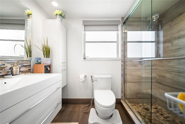 bathroom featuring toilet, wood finished floors, vanity, baseboards, and a stall shower