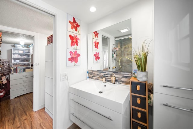 bathroom featuring tasteful backsplash, wood finished floors, vanity, and recessed lighting