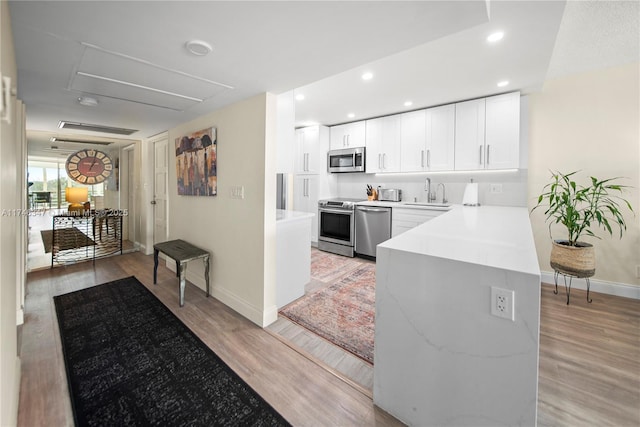 kitchen with light wood finished floors, light countertops, appliances with stainless steel finishes, white cabinets, and a sink