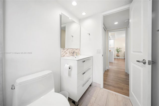 bathroom with toilet, recessed lighting, wood finished floors, vanity, and tasteful backsplash