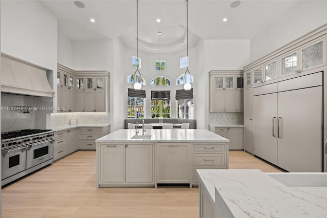 kitchen with sink, decorative light fixtures, gray cabinets, an island with sink, and range with two ovens