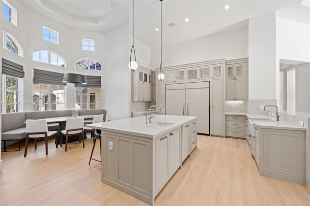 kitchen with sink, light wood-type flooring, paneled refrigerator, an island with sink, and pendant lighting