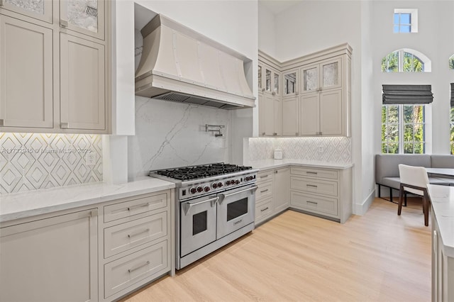 kitchen featuring light hardwood / wood-style flooring, double oven range, backsplash, light stone counters, and custom range hood