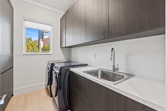 clothes washing area featuring sink, washer and clothes dryer, cabinets, light hardwood / wood-style floors, and ornamental molding