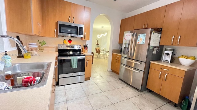 kitchen featuring light countertops, light tile patterned floors, appliances with stainless steel finishes, arched walkways, and a sink