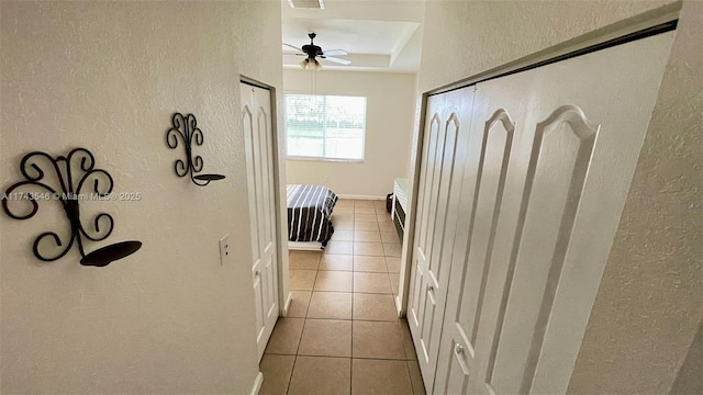 hallway with tile patterned flooring, visible vents, baseboards, a tray ceiling, and a textured wall