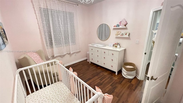 bedroom with baseboards, a crib, and wood finished floors