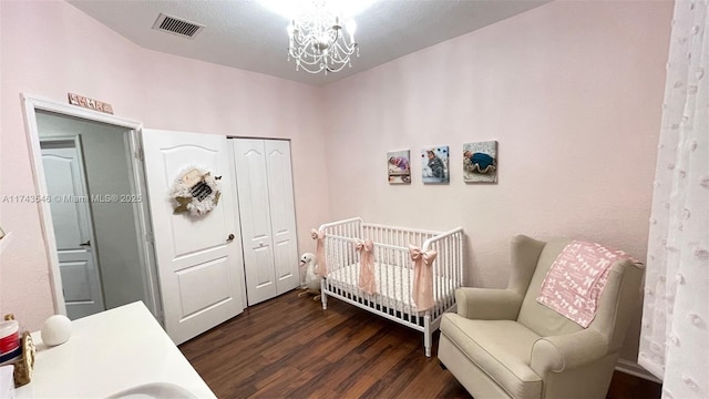 bedroom featuring wood finished floors, visible vents, a nursery area, a closet, and a notable chandelier