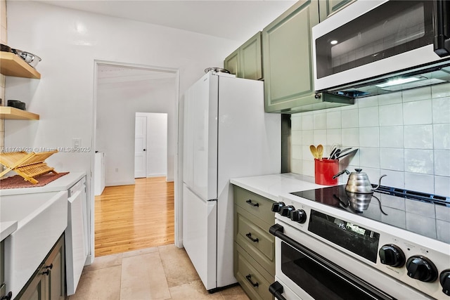 kitchen with green cabinetry, light tile patterned floors, white appliances, light stone countertops, and decorative backsplash