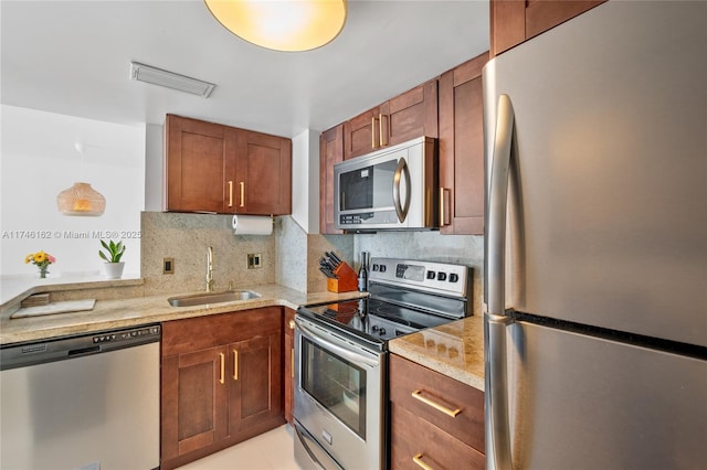 kitchen with sink, appliances with stainless steel finishes, tasteful backsplash, light stone countertops, and decorative light fixtures