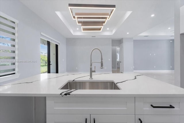 kitchen with light stone counters, sink, a raised ceiling, and white cabinets