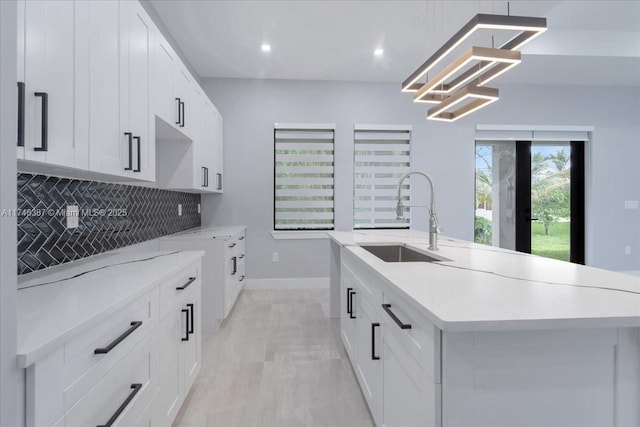 kitchen featuring sink, backsplash, white cabinets, and a center island with sink