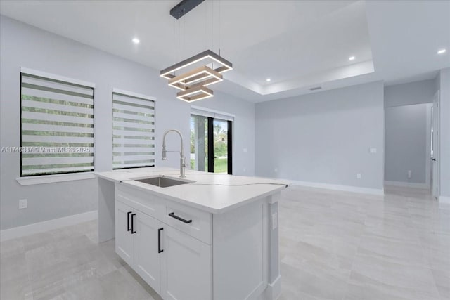 kitchen featuring sink, white cabinetry, hanging light fixtures, a tray ceiling, and a center island with sink