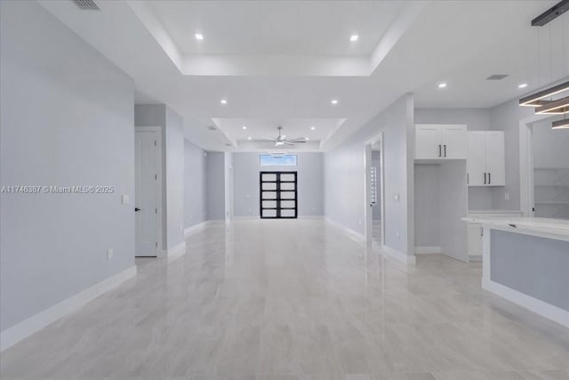 unfurnished living room with ceiling fan and a tray ceiling