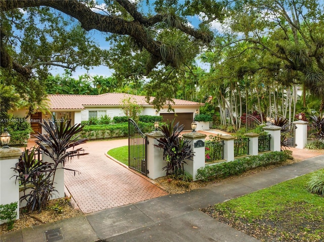 mediterranean / spanish-style house featuring a fenced front yard, a garage, decorative driveway, a gate, and stucco siding