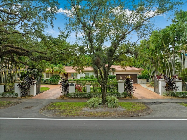 mediterranean / spanish home with a fenced front yard, decorative driveway, stucco siding, a garage, and a tiled roof