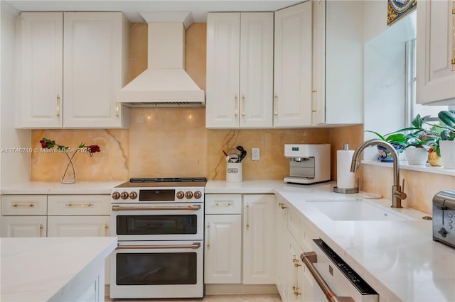 kitchen with range with two ovens, dishwashing machine, premium range hood, white cabinetry, and a sink