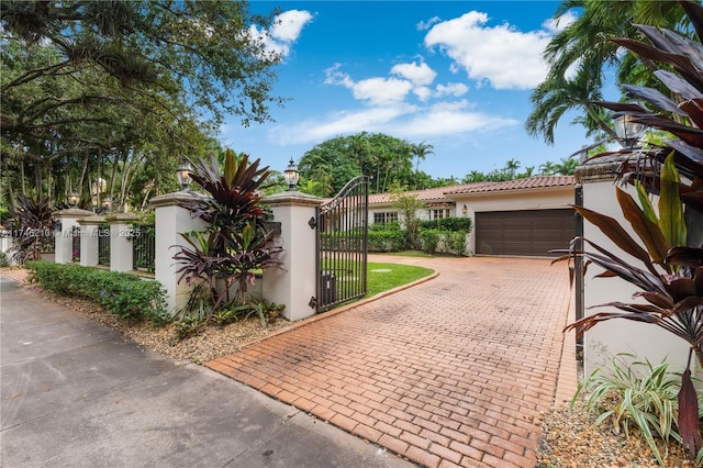 mediterranean / spanish home featuring a fenced front yard, a garage, decorative driveway, a gate, and stucco siding