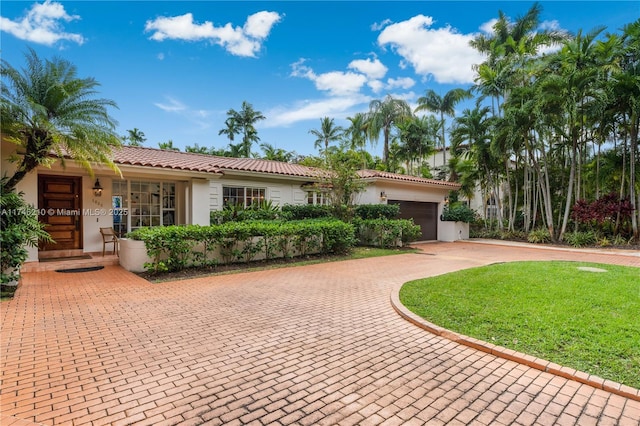 view of front of home featuring decorative driveway, a tile roof, stucco siding, an attached garage, and a front lawn