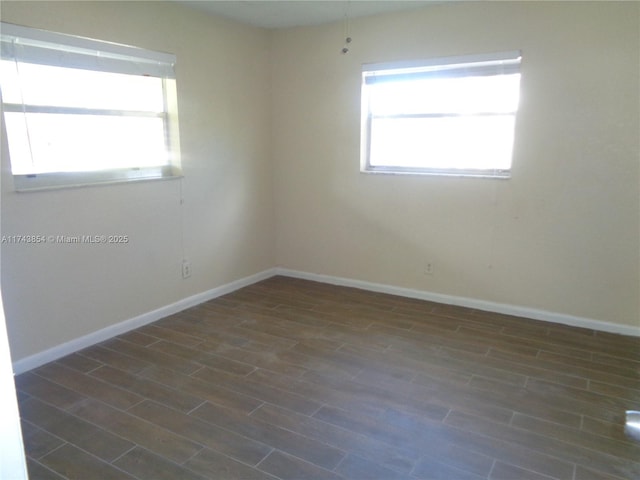 spare room with baseboards and dark wood-style flooring