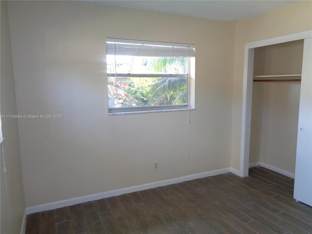 unfurnished bedroom featuring a closet, dark wood-style flooring, and baseboards