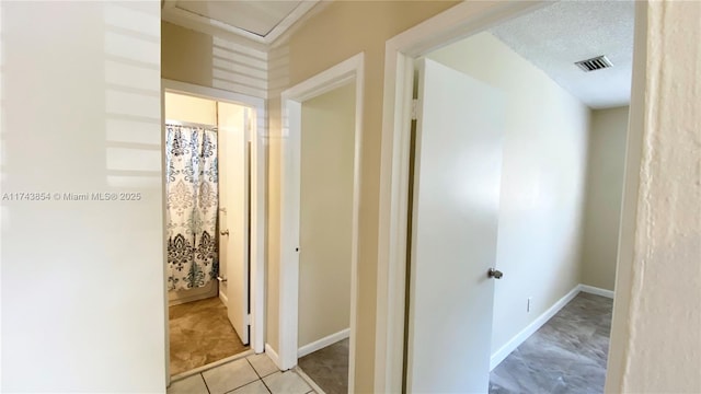 hallway with a textured ceiling, light tile patterned floors, visible vents, and baseboards