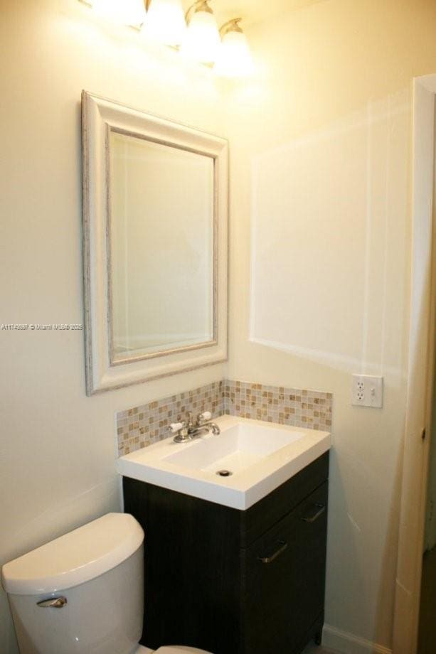 bathroom featuring vanity, toilet, and backsplash