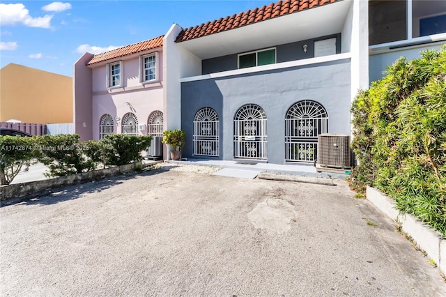 view of exterior entry featuring stucco siding, a tile roof, fence, and central air condition unit