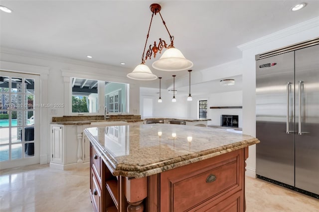 kitchen featuring sink, stainless steel built in refrigerator, light stone counters, a kitchen island, and decorative light fixtures