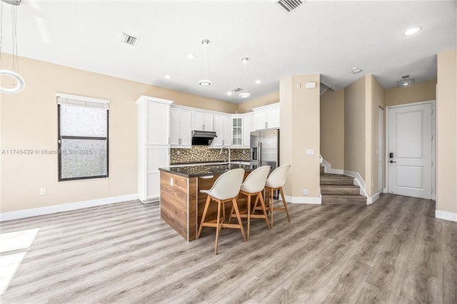 kitchen featuring an island with sink, white cabinetry, hanging light fixtures, and dark stone countertops