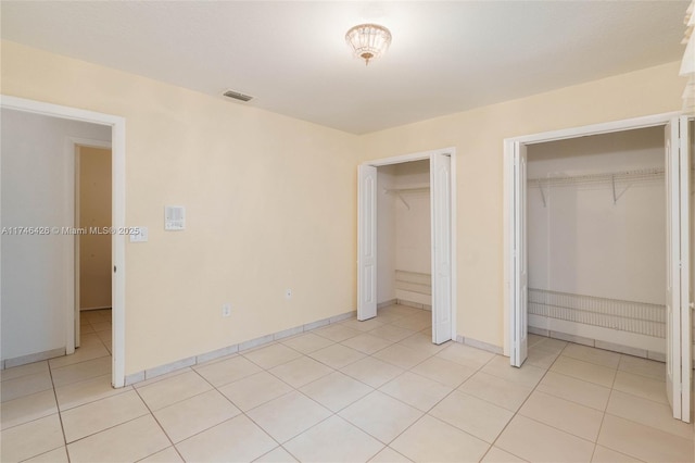 unfurnished bedroom featuring light tile patterned floors and two closets